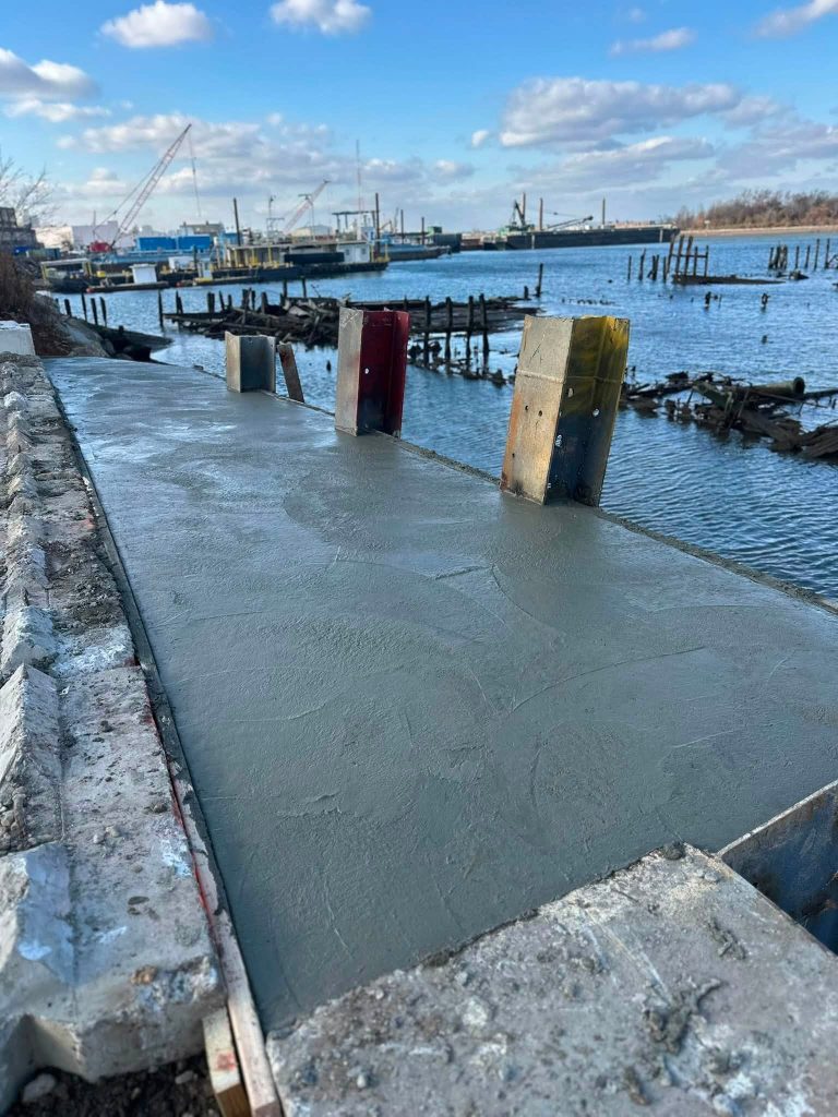 Freshly poured concrete bulkhead cap with steel piling brackets along the Staten Island waterfront