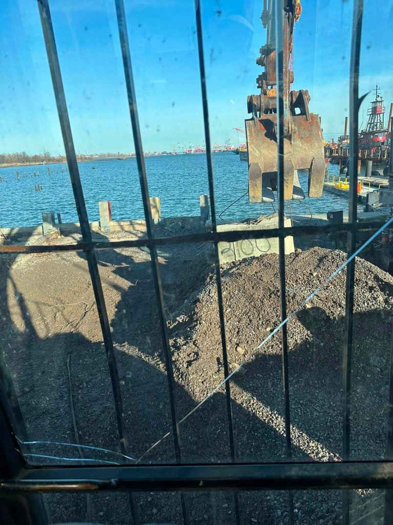 Excavator clamshell bucket moving fill material during waterfront grading in Staten Island