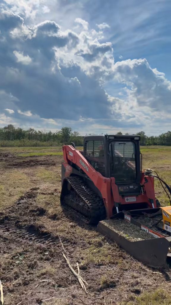 Kubota skid steer with mulching attachment working the cleared bog under a cloudy sky