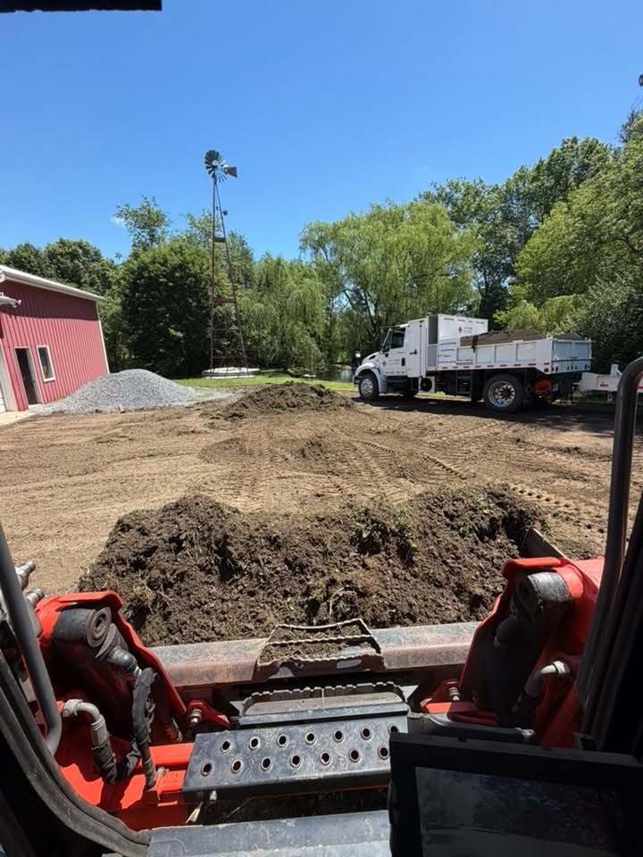 Skid steer regrading a stone parking area with fresh gravel piles staged nearby