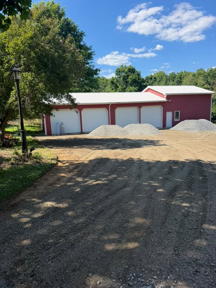 Fresh gravel piles staged for a parking area restoration in front of a pole barn