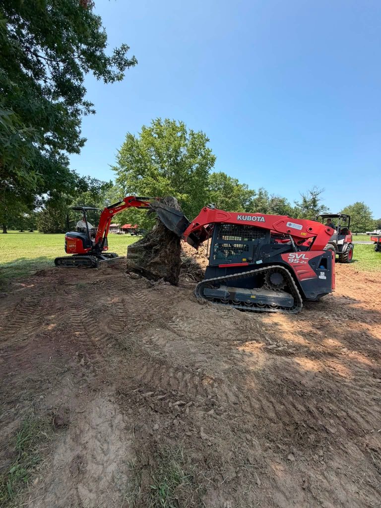 Mini excavator and skid steer working together to pull a large tree stump from the ground